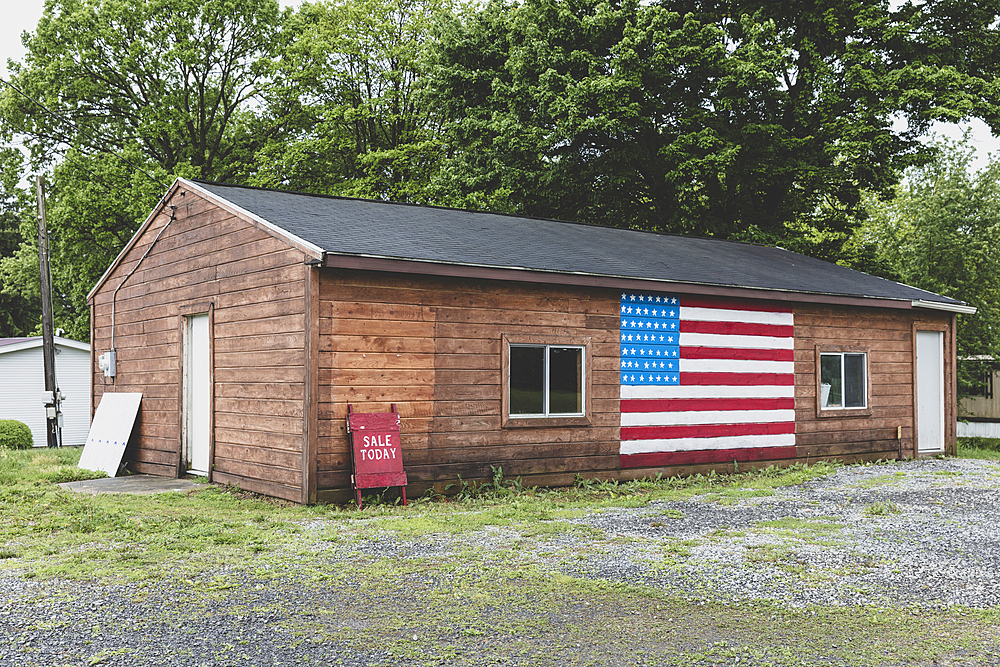 A Sale Today A board and an American flag painted on empty building on a street in a small town.