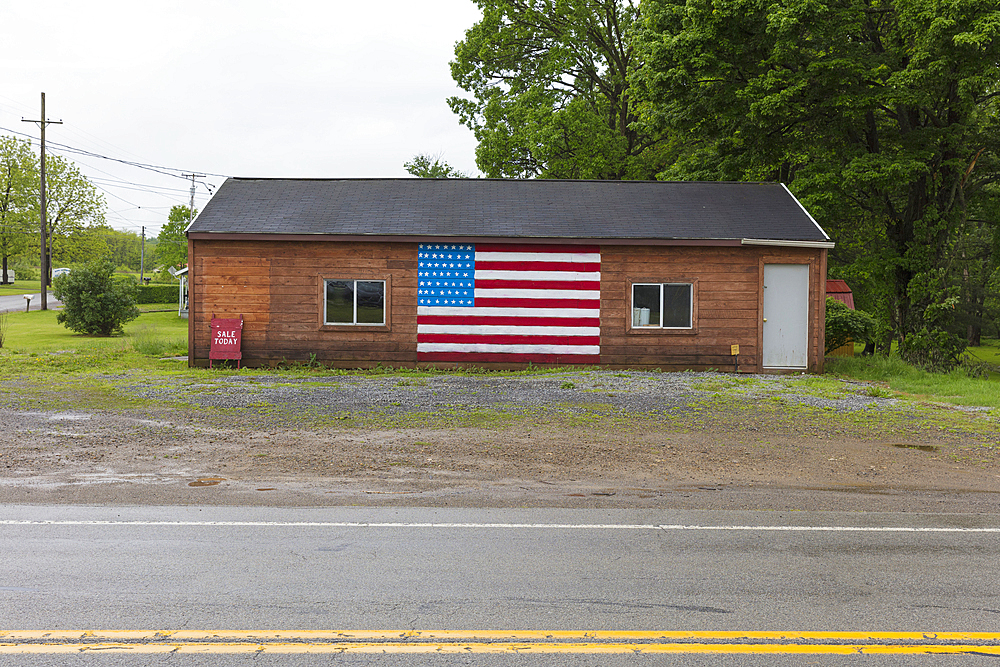 A Sale Today A board and an American flag painted on empty building on a street in a small town.