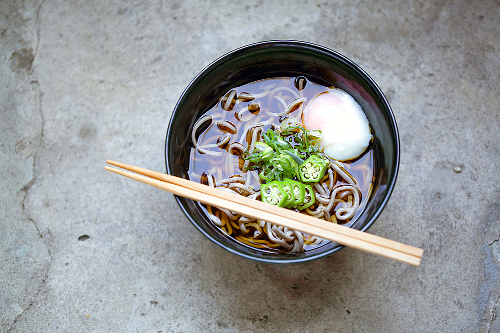 A black china bowl of noodles and broth with sliced chillis and an egg.