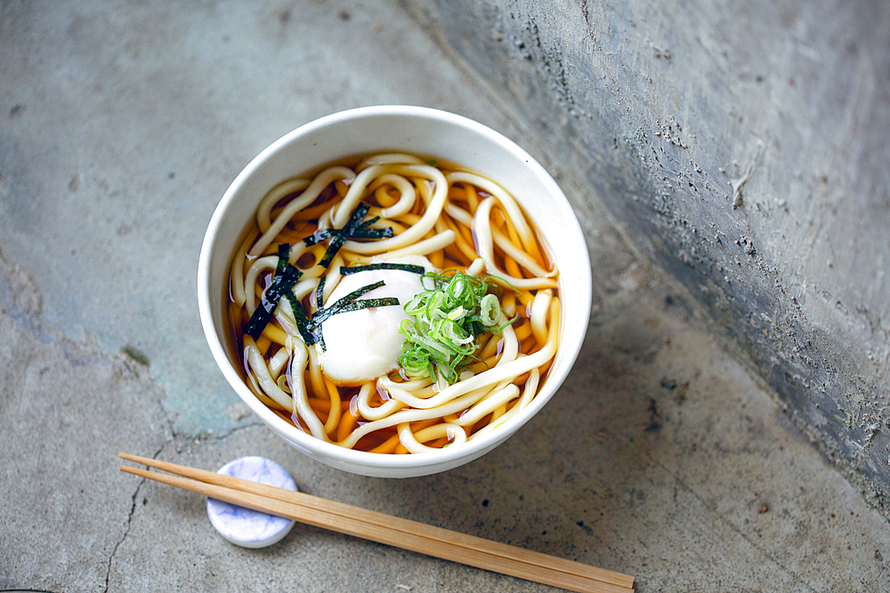 A bowl of noodles, vegetables and broth and a set of chopsticks.