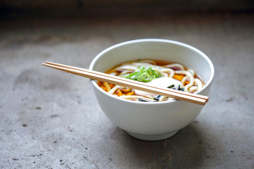 A bowl of noodles, vegetables and broth and a set of chopsticks.