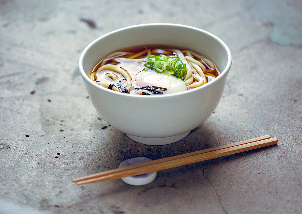 A bowl of noodles, vegetables and broth and a set of chopsticks.