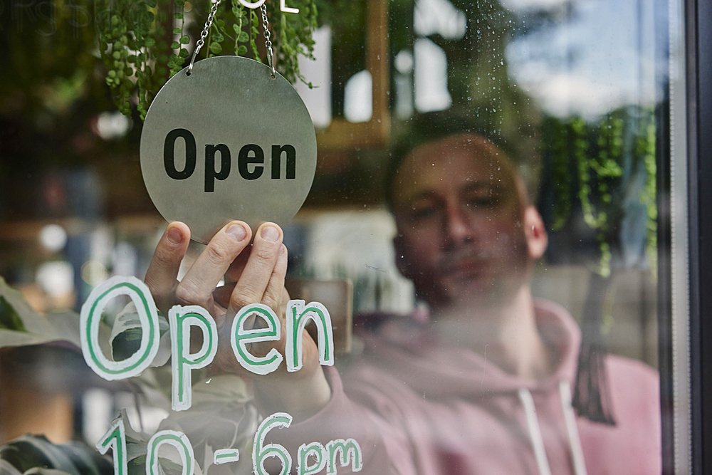 Man placing Open sign in window of shop