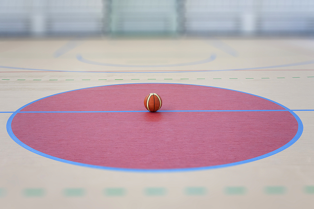 A school sports hall with a marked indoor football pitch, a striped blue and yellow ball in a pink circle.