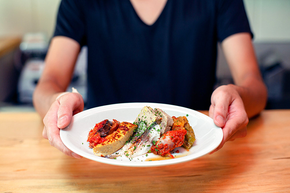 A man standing at a restaurant counter presenting plates of cooked food, menu dishes.