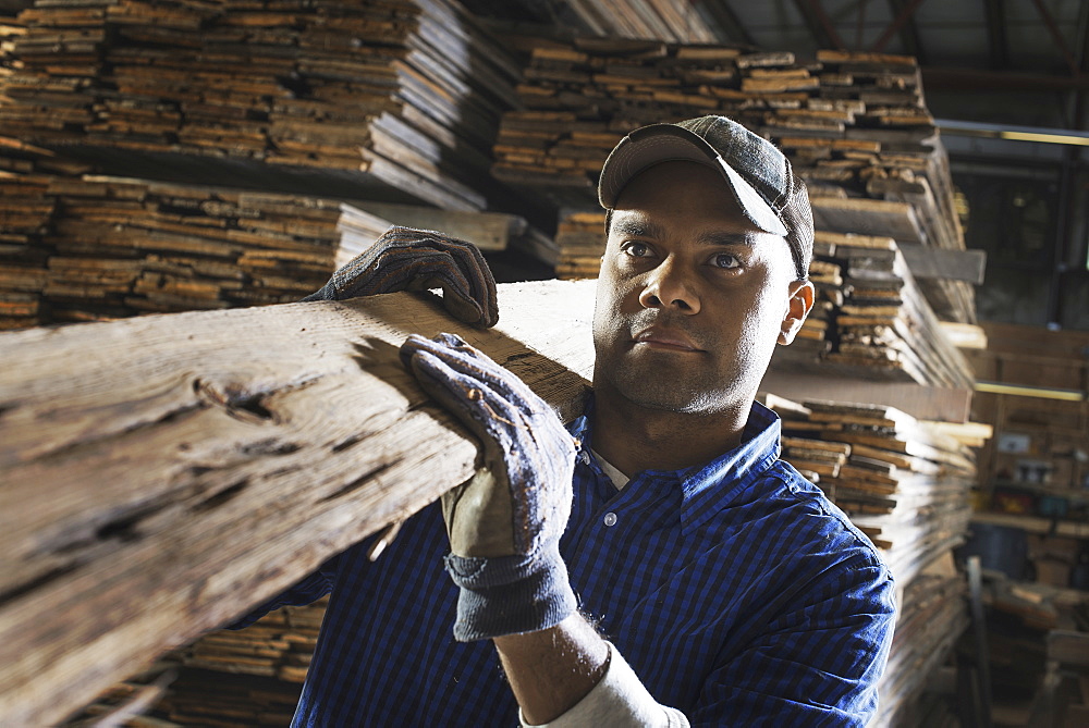 A heap of recycled reclaimed timber planks of wood. Environmentally responsible reclamation in a timber yard. A man carrying a large plank of splintered rough wood, Pine Plains, New York, USA