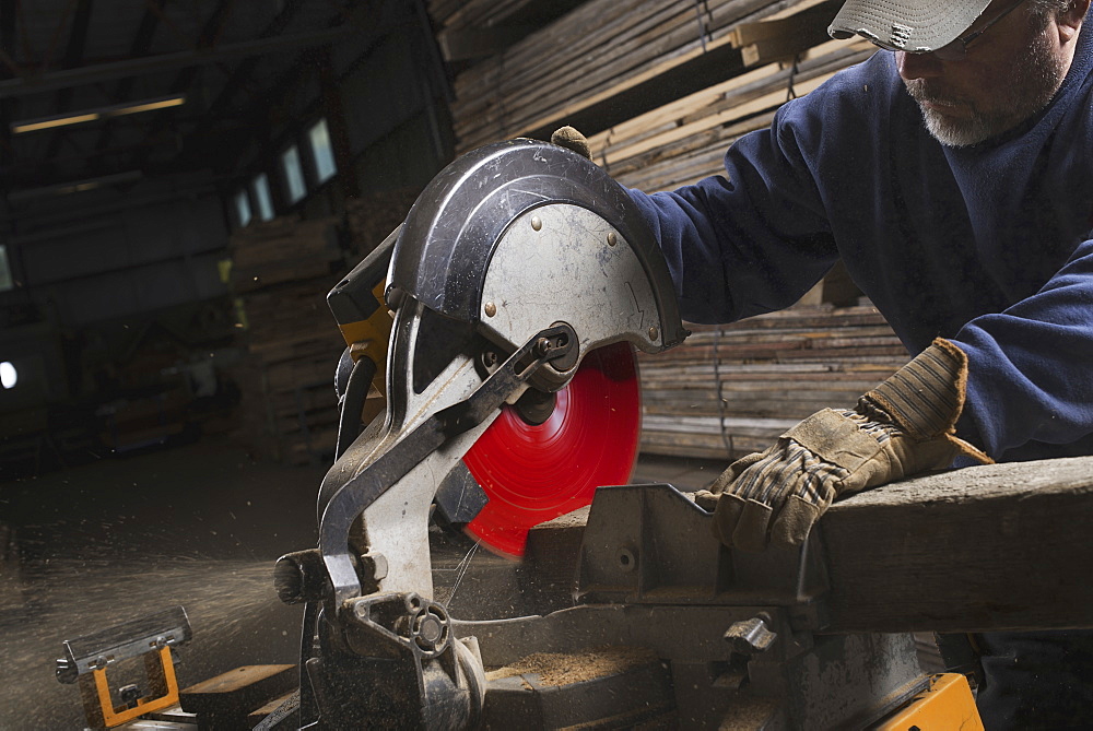 A reclaimed lumber workshop. A man in protective eye goggles using a circular saw to cut timber, Woodstock, New York, USA