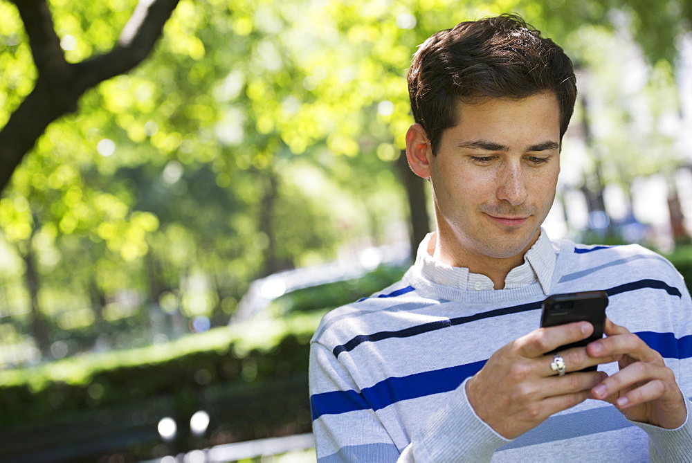 Summer in a city park. Business people on the move. A man checking his smart phone for messages. 