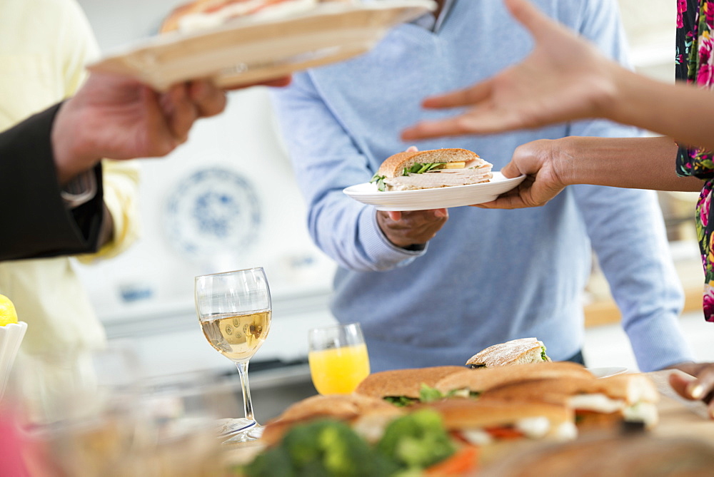 A group of people gathering for a party and a meal. An informal office party or networking social event. People handing plates of food across a buffet table.