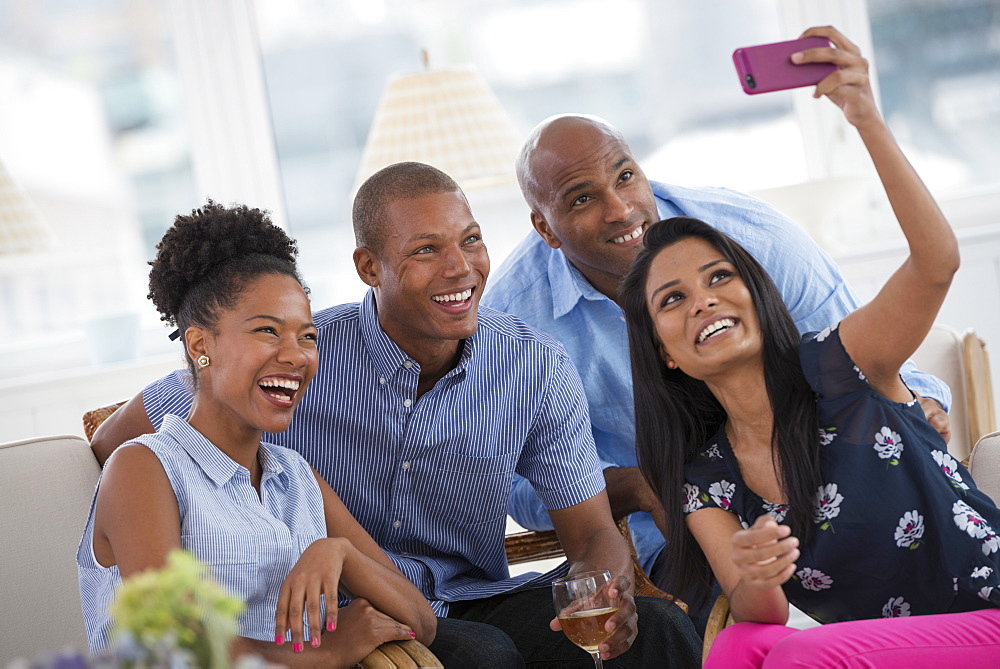 A group of people gathering together for a party or an office event. A woman taking a selfie of the group with a pink smart phone.