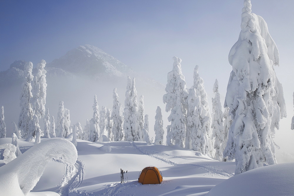 A bright orange tent sits on a snowy ridge overlooking a mountain in the distance, Cascade Mountains, Washington, USA