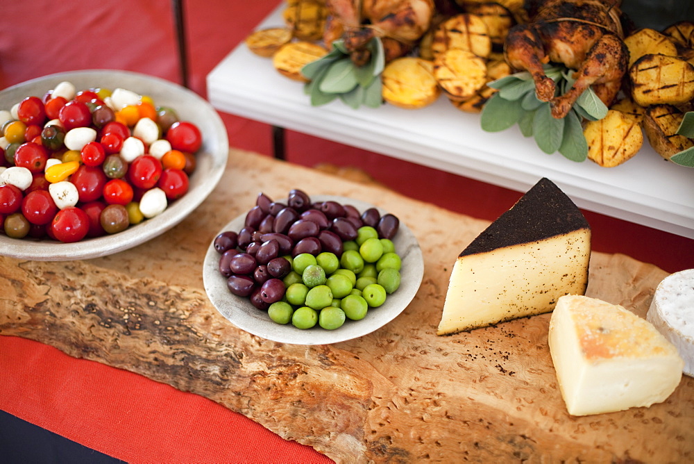 Organic food presented on white dishes for a party. Cheese, free range chicken, heritage tomatoes and salad ingredients. Farmstand foods, Salt Lake City, Utah, USA