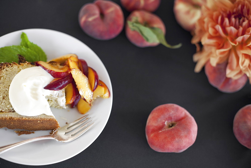 A table viewed from overhead. Organic fruit, peaches, and flowers. a plate with fresh fruit, cake and creme fraiche. A fork. Dessert, Park City, Utah, USA