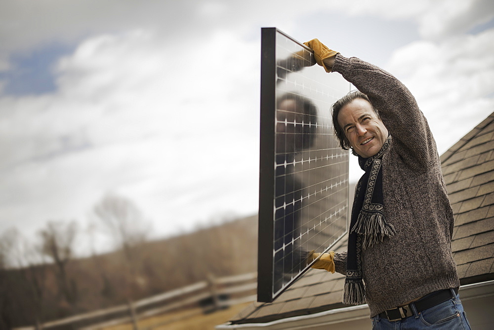 A man carrying a large solar panel across a farmyard, Cold Spring, New York, USA