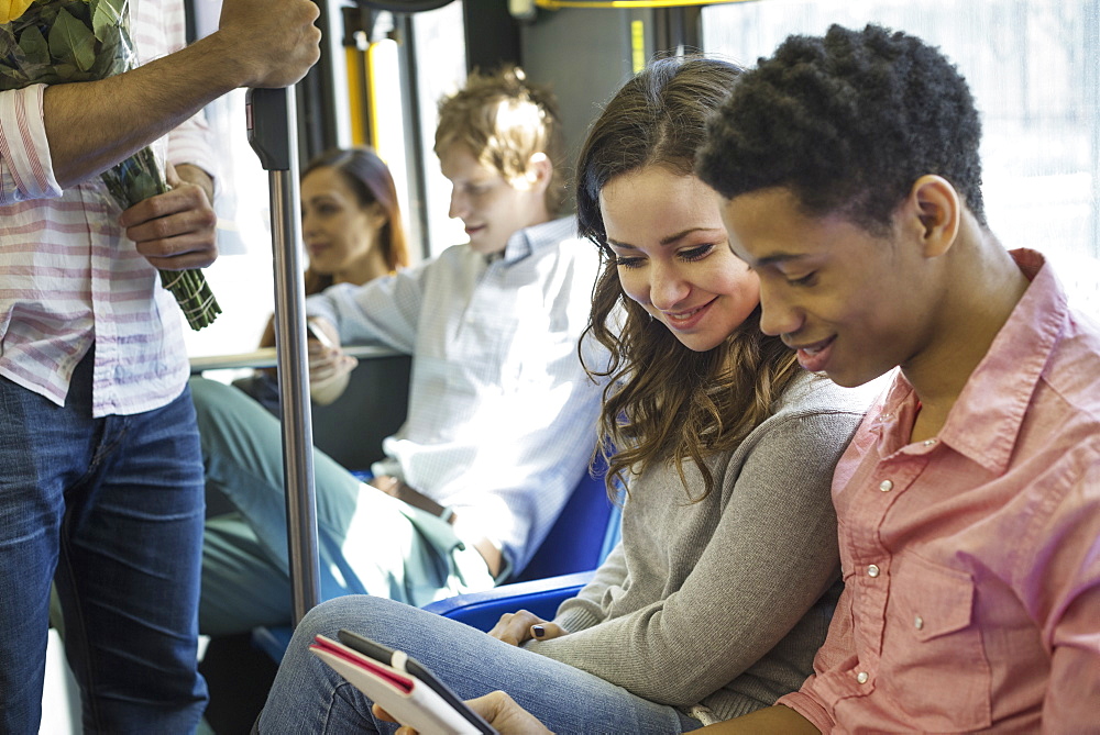 Urban Lifestyle. A group of people, men and women on a city bus, in New York city. A couple side by side looking at a digital tablet, New York city, USA