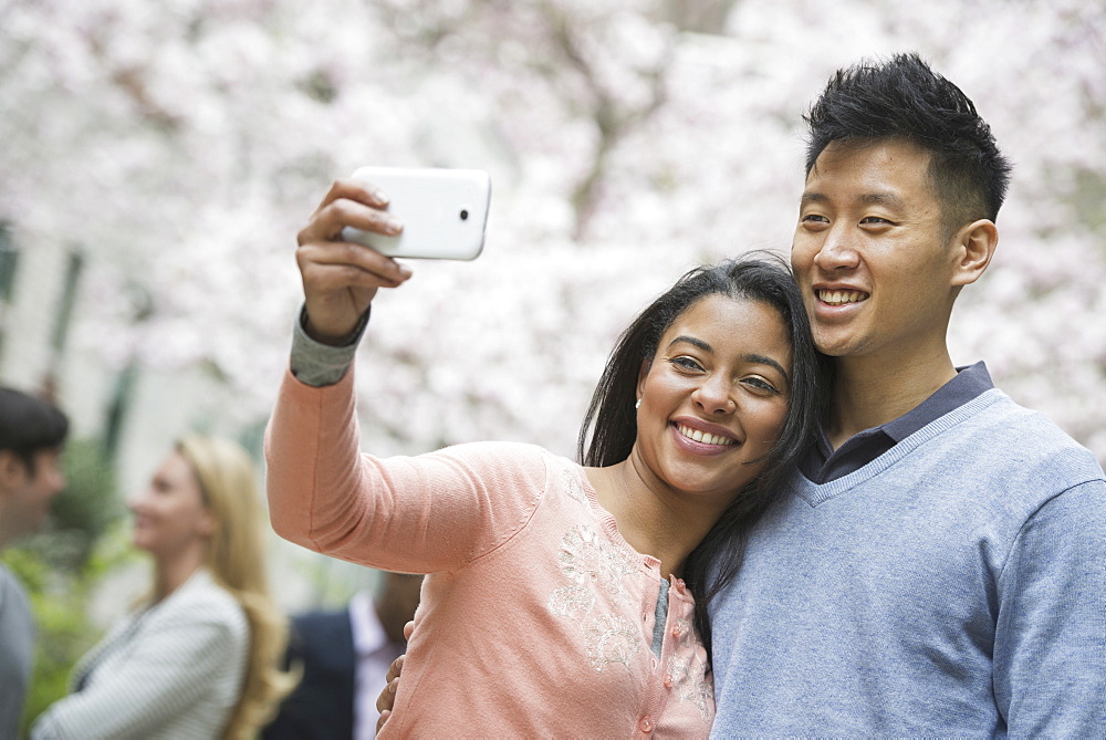 City life in spring. Young people outdoors in a city park. A couple taking a self portrait or selfy with a smart phone, New York city, USA