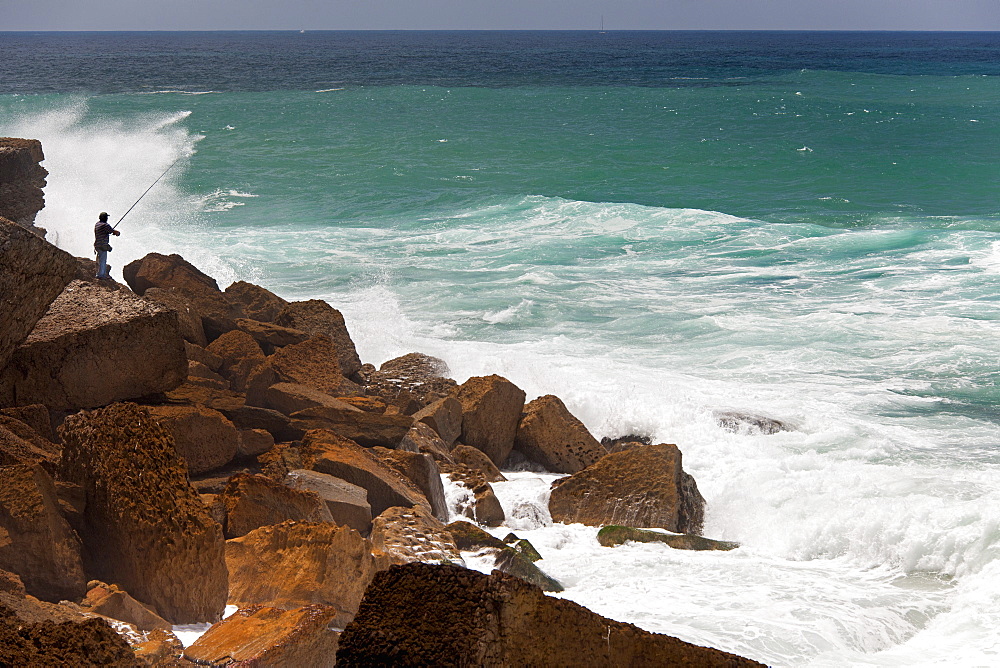 A fisherman standing on the rocks surf casting in the white waves on the Antlantic coast, Azenhas do Mar, Atlantic Coast, Portugal