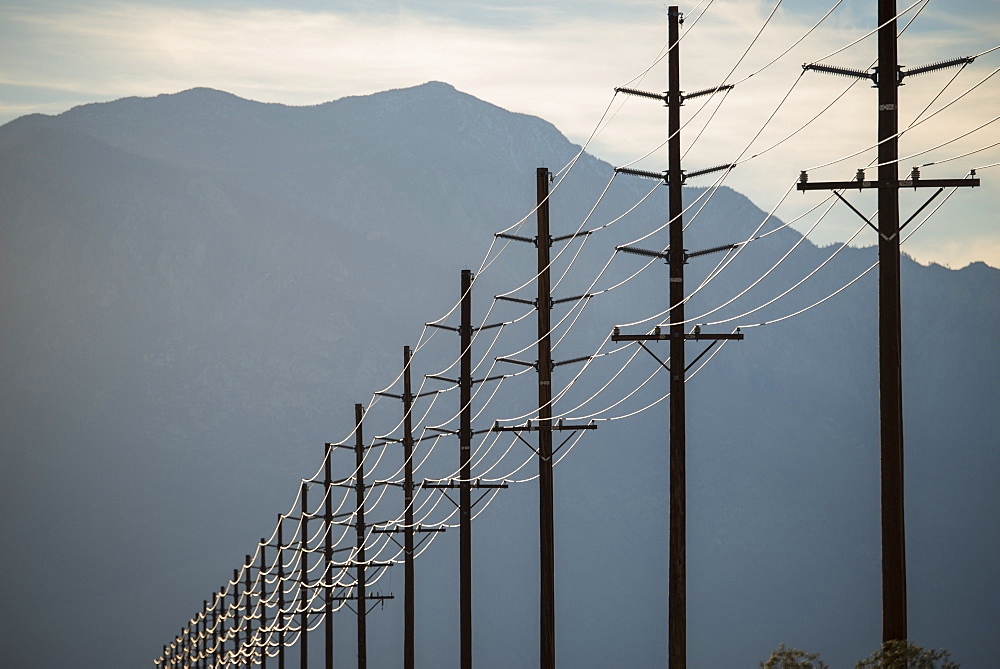 Power lines in rows across the landscape, against a mountain and sunset sky, California, USA