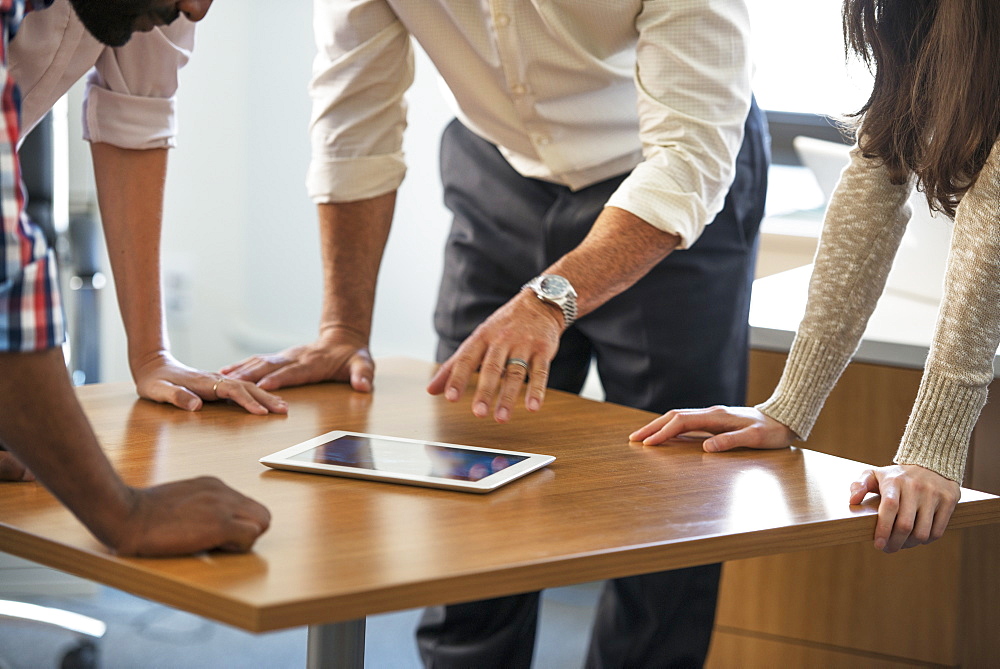 Four people leaning on a table at a meeting, looking at a digital tablet