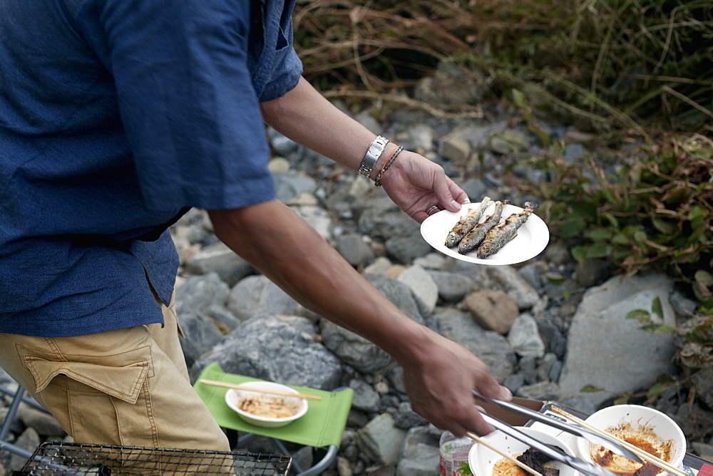 Man holding a plate of grilled fish at a picnic, Kyoto, Honshu Island, Japan