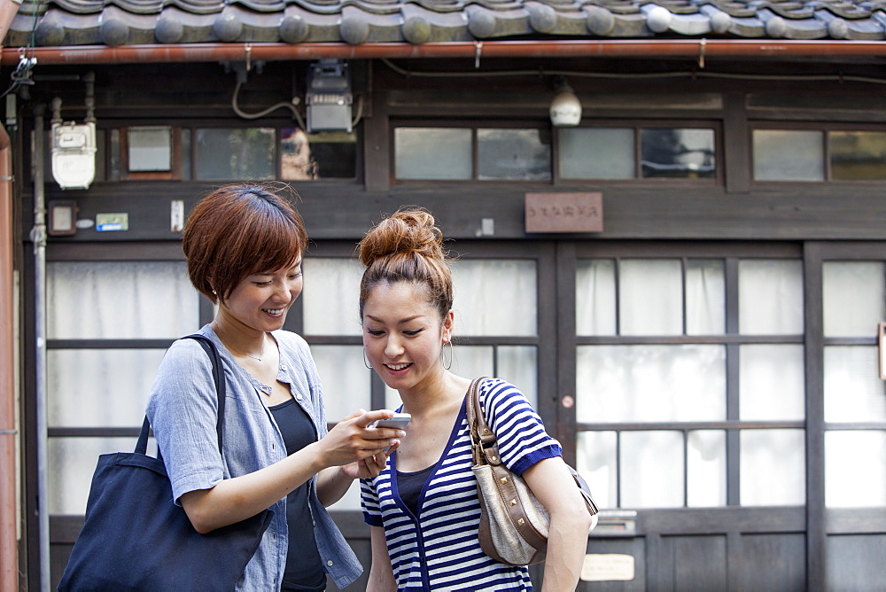 Two women standing outdoors, looking at cellphone, Osaka, Japan