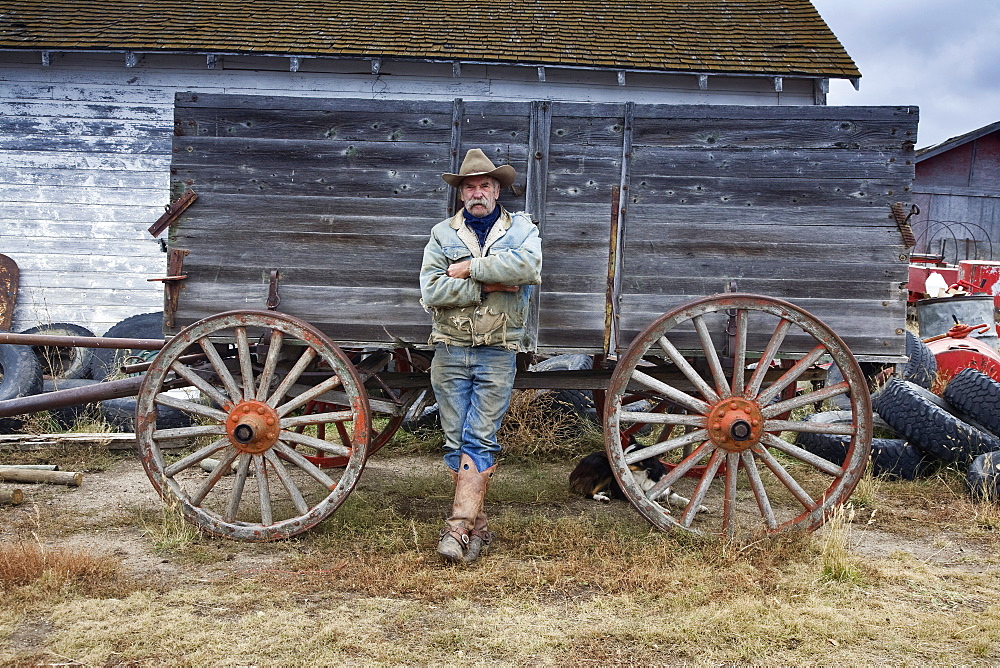 Man in cowboy hat and cowboy boots leaning against a wooden wagonCowboy, Saskatchewan, Canada