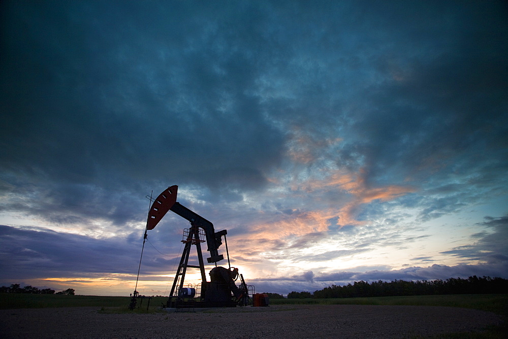 An oil derrick, a well head pump arm with frame, silhouetted against the evening sky. Oil business, Oil field pumpjack, Saskatchewan, Canada