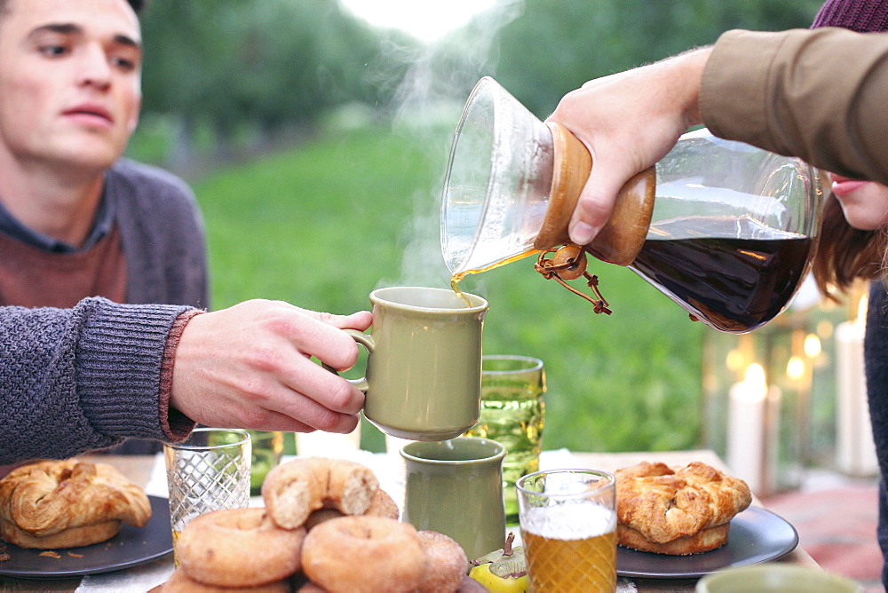 An apple orchard in Utah. Group of people sitting round a table with food and drink, pouring coffee, Sataquin, Utah, United States of America