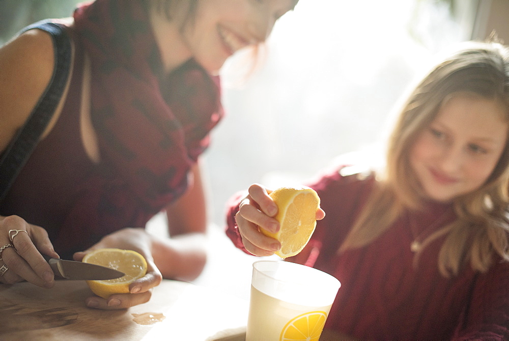 A woman and a girl sitting at a table, girl squeezing the juice from a lemon into a glass, Woodstock, New York State, USA