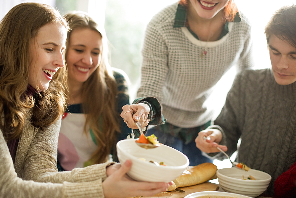 Four people sitting and standing at a table, a woman serving food into a bowl, Woodstock, New York State, USA