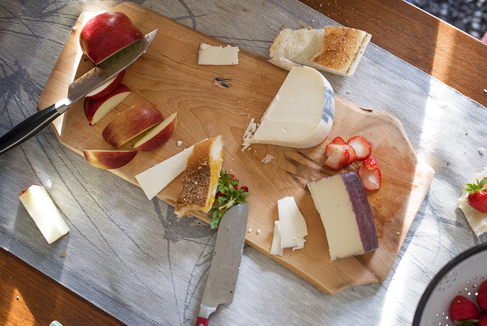 Knives and a wooden chopping board with a selection of cheeses, apples and bread, Woodstock, New York State, USA