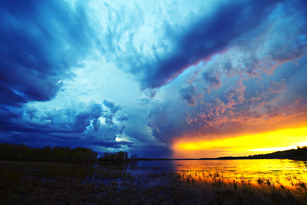 Sunset on the horizon over a lake, and storm clouds rising, Saskatchewan, Canada