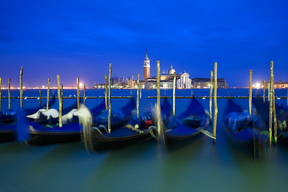 A view from the Riva degli Schiavoni and the Piazza San Marco across the water to the island and church of San Giorgio Maggiore, Gondolas moored at dusk, Venice, Italy