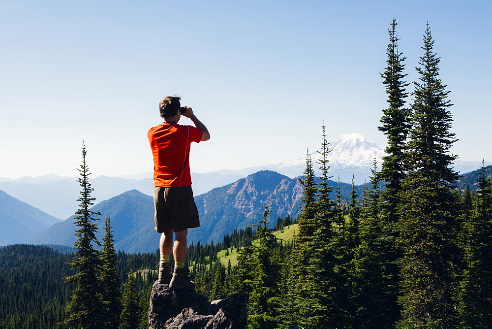 A man standing on a mountain ridge, taking a photograph of the landscape, Skamania County, Washington, USA