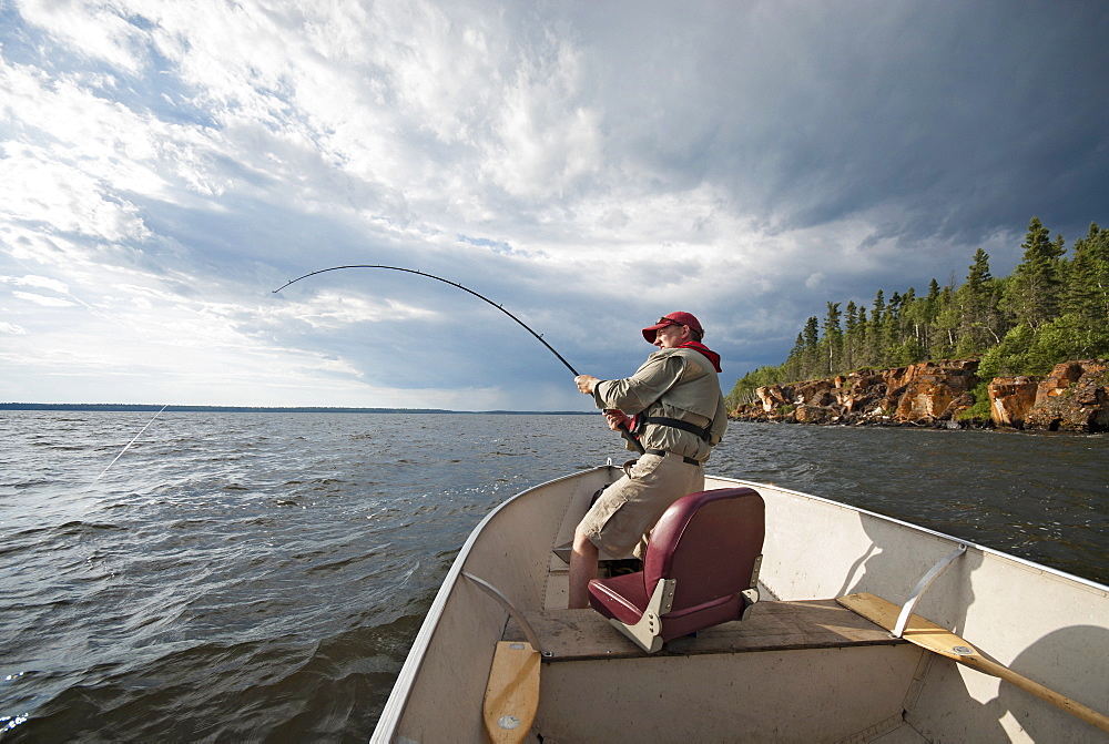 A man fishing from an open boat offshore, A fish on the line, The fishing rod bending from the weight, USA