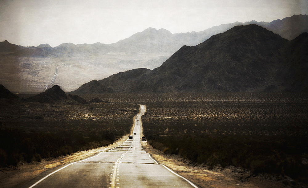 A road leading into the distance, to a range of mountains. Desert scenery, cars on the road, California, United States of America