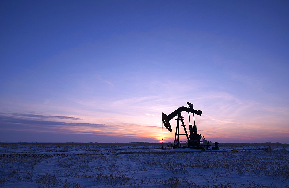 An oil drilling rig and pumpjack on a flat plain in the Canadian oil fields at sunset, Canada