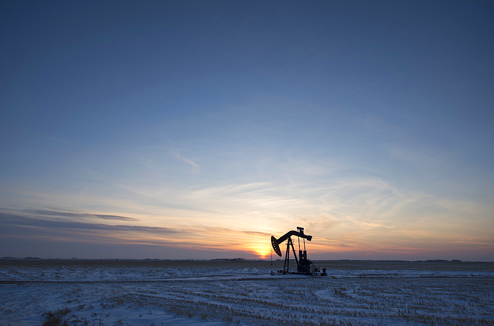 An oil drilling rig and pumpjack on a flat plain in the Canadian oil fields at sunset, Canada