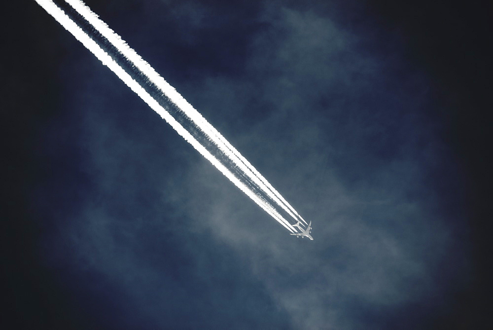 A jet with a clear condensation or vapour trail or contrail across a dark blue sky