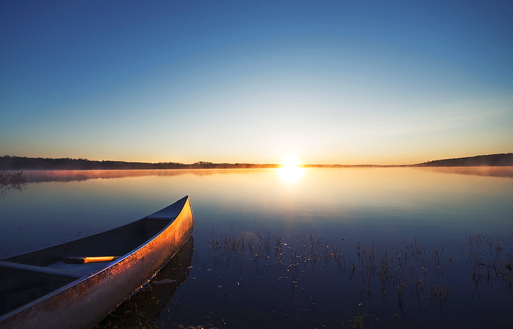 A canoe on a flat calm lake at sunset, Kenosee Lake, Saskatchewan, Canada