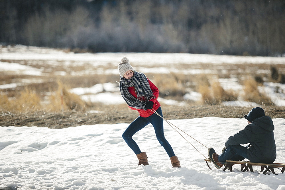 A brother and sister in the snow, one pulling the other on a sledge, Mountains, Utah, USA