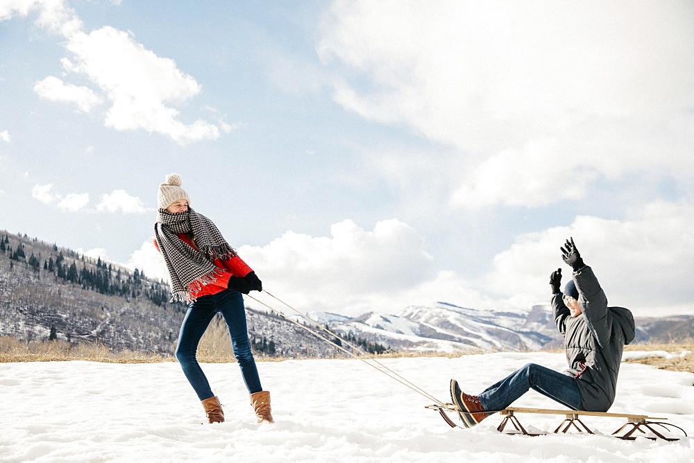 A young girl pulling her brother on a sledge through the snow, Mountains, Utah, USA