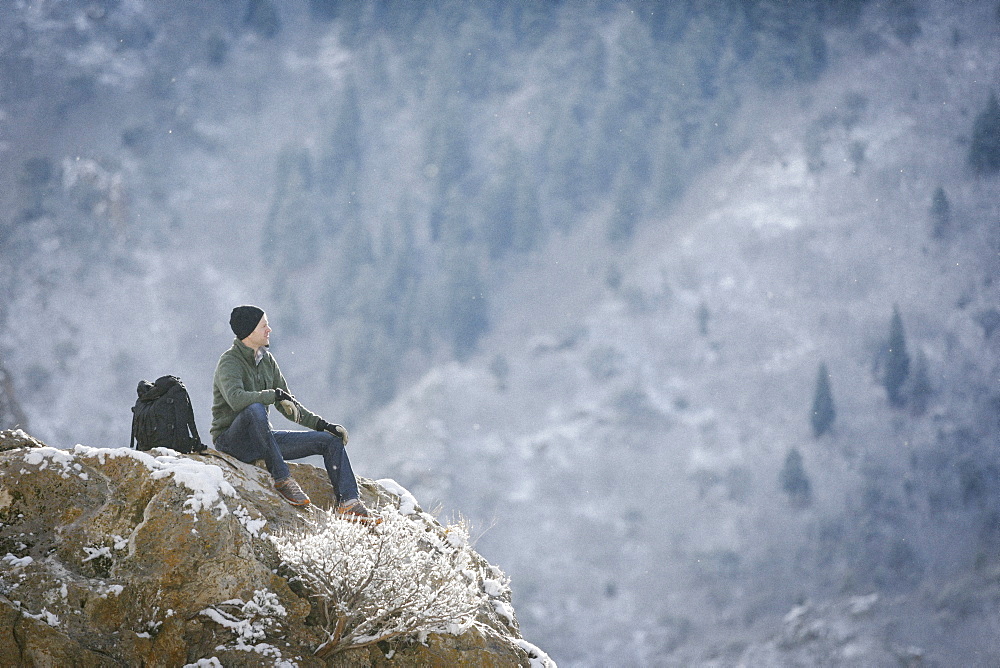 A man, a hiker in the mountains, taking a rest on a rock outcrop above a valley, Mountains, Utah, USA