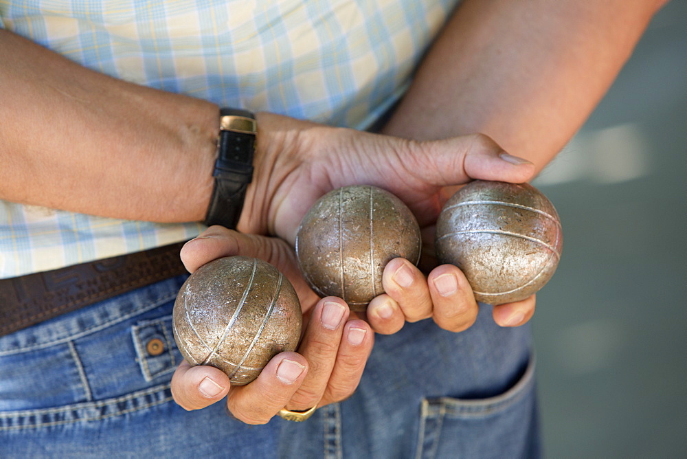 A boules player holding three metal boules in his hands behind his back, Boules player, France