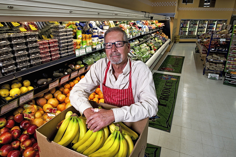 A man standing in a grocery shop beside a display of fresh fruits and vegetables.