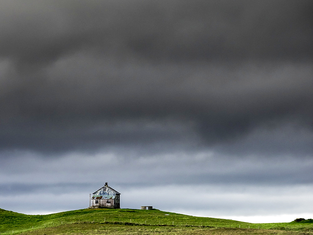 A barn on the crest of a hill, and dark storm clouds glowering over the land, Iceland