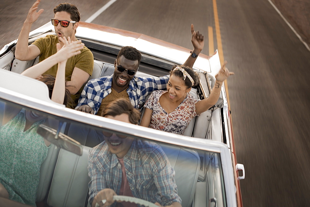 A group of friends in a red open top convertible classic car on a road trip, United States of America