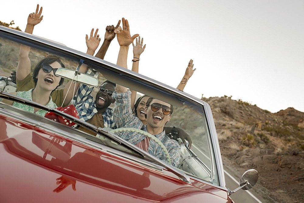 A group of friends in a red open top convertible classic car on a road trip, United States of America