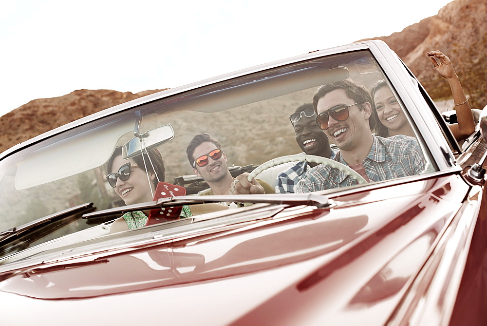 A group of friends in a red open top convertible classic car on a road trip, United States of America