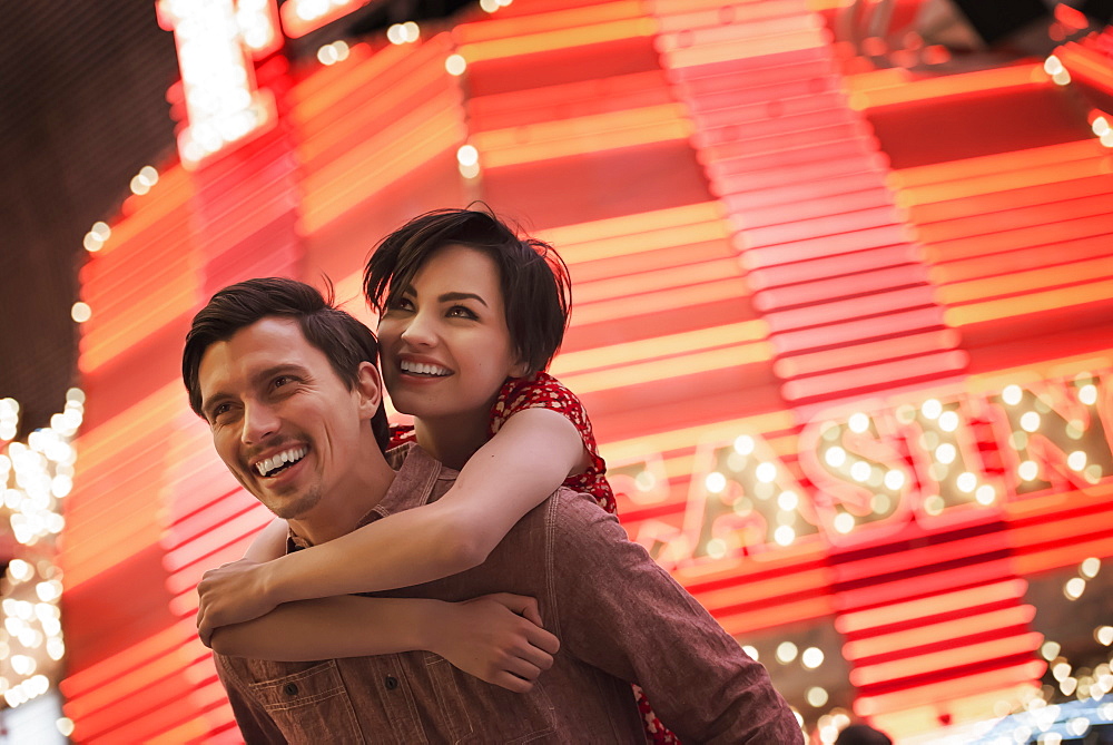 A man giving a woman a piggyback, under a bright neon Casino sign, United States of America